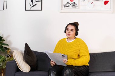 Ayrıca boyunda bir kadın kanepeye uzanır, süveter ve kulaklık giyer, işine odaklanır..