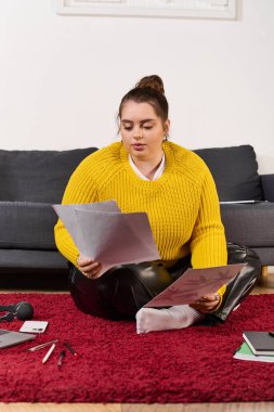 Ayrıca kırmızı halıya oturmuş ofis malzemeleriyle çevrili kağıtları inceliyor..