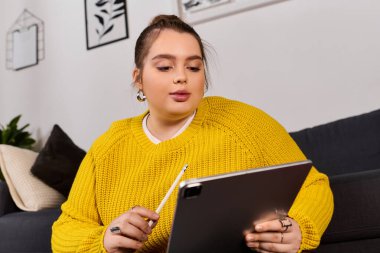 Artı, parlak sarı kazaklı boyunda bir kadın sıcak, davetkar bir yerde tabletine odaklanmış..