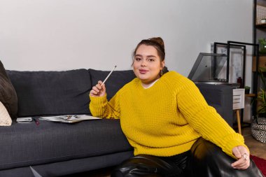 Güzel ve iri yarı bir kadın kanepeye uzanıp düşünceli bir ifadeyle sanat yaratıyor..