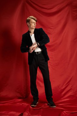 Genç, çekici bir adam modern erkeksiliği sergiliyor, kendine güvenen şık bir elbise içinde duruyor..