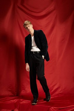 Kendine güvenen genç bir adam modern modayı parlak kırmızı bir arka plana karşı modelliyor..