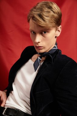 Çarpıcı özellikleri olan genç bir adam canlı kırmızı bir arka plana karşı poz veriyor, modern erkekliği somutlaştırıyor..