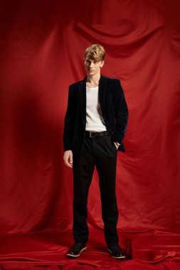 Şık bir genç adam, kırmızı bir zemine karşı kadife bir ceketle modern erkeksiliği yayıyor..