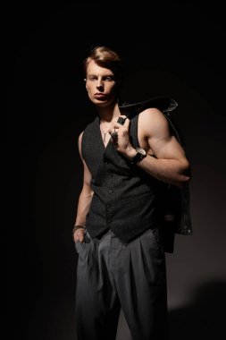 Genç, çekici bir adam loş bir ortamda, kendinden emin bir şekilde duruyor, modern erkeklik fışkırıyor..