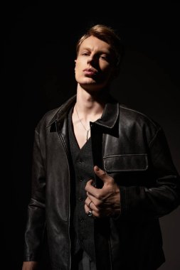 Genç bir adam karanlıkta kendinden emin bir şekilde duruyor, modern erkekliğin vücut bulmuş hâli..