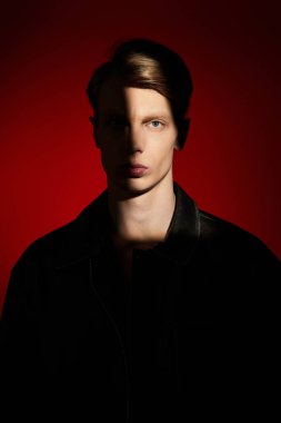 Genç bir adam kendinden emin duruyor, yüzünde dramatik gölgelerle poz veriyor..