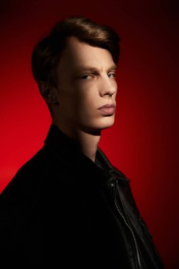 Belirli özelliklere sahip kendine güvenen genç bir adam cesur bir kırmızı zemine karşı duruyor..