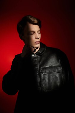 Yakışıklı genç bir adam canlı kırmızı bir arka plana karşı özgüvenle poz veriyor, modern erkekliğin vücut bulmuş hali..