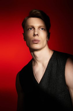 Çekici özellikleri olan genç bir adam, tarzını vurgulayan koyu kırmızı bir arkaplan ile özgüvenle poz verir..