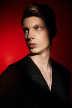 Genç bir adam, canlı kırmızı bir arka plana yoğun bir bakışla modern erkeklik sergiliyor..