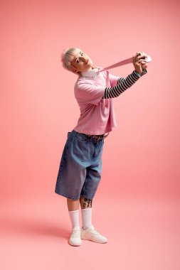 Güzel genç bir kadın, yumuşak pembe bir arka planda duruyor, neşeyle esneyen bir sakız..