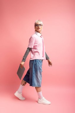 Genç bir kadın kendine güvenerek parlak pembe bir zeminde yürüyor, eşsiz tarzıyla hava atıyor..