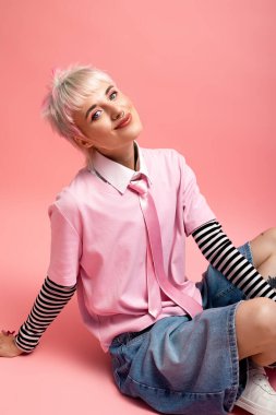 Kısa saçlı, pembe giyinmiş, neşeyle yerde oturan genç bir kadını resmediyor..