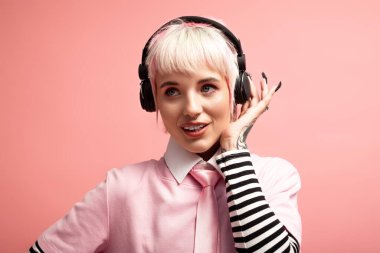 Canlı pembe bir ortamda, genç bir kadın kulaklığı açık bir şekilde gülümser ve müzikten zevk alır..