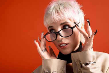 Genç bir kadın gözlüğünü ayarlıyor, modern saç stilini ve kendine güvenen ifadesini sergiliyor..