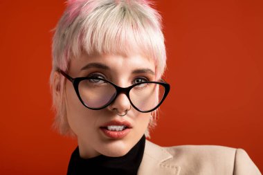 Canlı turuncu bir ortamda, kendine güvenen genç bir kadın şık gözlükleriyle eşsiz tarzını sergiliyor..