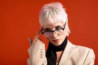 Genç bir kadın şık saç stili ve gözlükleriyle düşünceli bir şekilde poz veriyor..