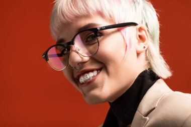 Genç bir kadın benzersiz tarzını renkli saçlarıyla, modaya uygun gözlükleriyle ve parlak bir gülümsemesiyle sergiliyor..