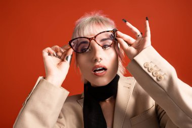 Şık bir genç kadın canlı bir arkaplanda poz veriyor, moda gözlükler takıyor ve giyiniyor..