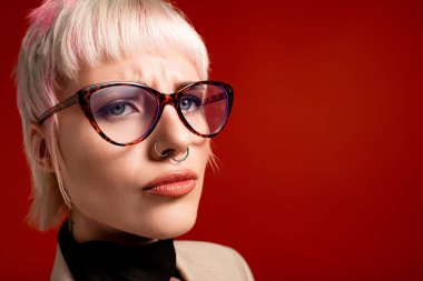 Genç bir kadın kendine has tarzını sergilerken kalın gözlükler takıyor ve kendine güvenen bir ifade takınıyor..