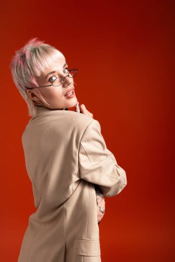 Kısa saçlı ve gözlüklü kendine güvenen genç bir kadın zarif bir şekilde ayakta duruyor ve güzelliğini ön plana çıkarıyor..