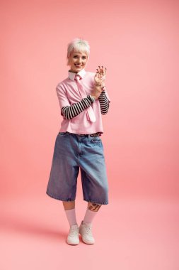 Genç bir kadın canlı pembe bir arka plana karşı mutlu bir şekilde duruyor..