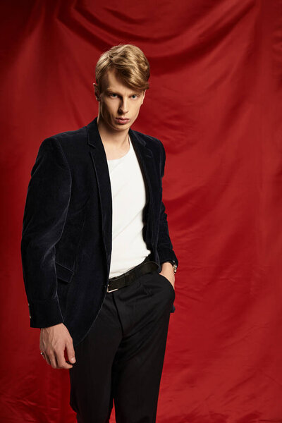 A young, handsome man stands confidently dressed in stylish attire, offering an alluring presence.