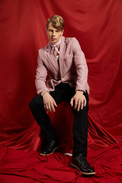 Стильный молодой человек уверенно позирует против глубокой красной ткани, демонстрируя современные модные тенденции.