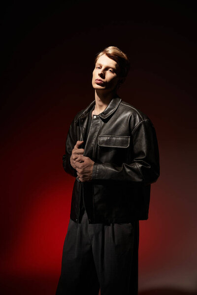 A confident young man in a stylish outfit stands against a moody backdrop, embodying masculinity.