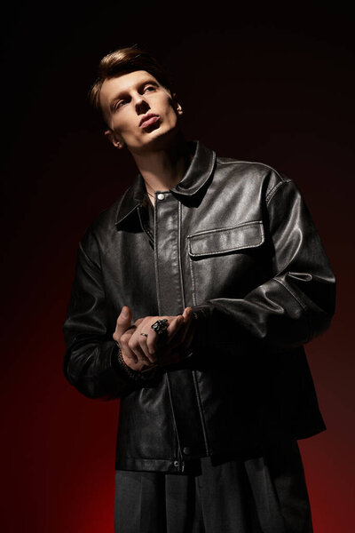 Young man stands confidently, showcasing modern fashion and allure in dramatic lighting.