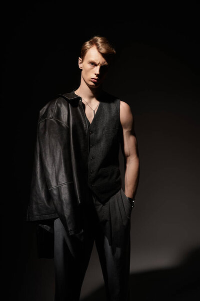 A handsome young man stands confidently in a dimly lit space, showcasing modern masculinity.