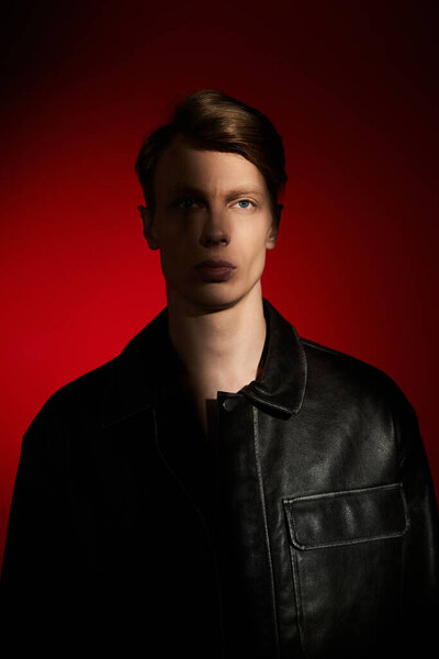 A handsome young man stands tall, embodying modern masculinity in a bold red setting.