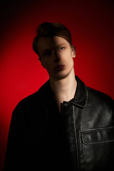 Молодой человек уверенно стоит на ярком красном фоне, демонстрируя современную мужественность.