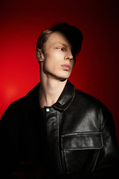 Young man exudes modern masculinity while striking a fashionable pose under bold lighting.