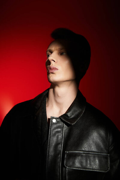 A young, handsome man exudes confidence in a dark jacket under warm light.