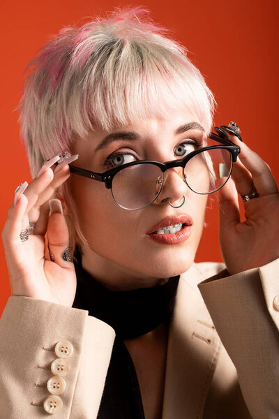 Ярко освещенный портрет красивой молодой женщины, регулирующей свои очки, излучающей шарм и стиль.