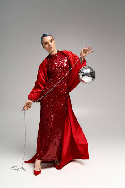 A young woman in a red gown gracefully holds a disco ball, exuding festive spirit.