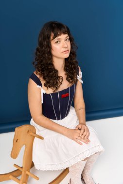 Zarif giyinmiş genç bir kadın sakin bir ortamda sallanan bir atın üzerinde poz veriyor..