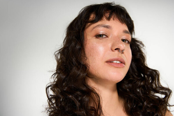 A confident young woman with curly hair poses stylishly in a bright studio.