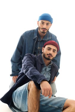 Moda kıyafetleri giymiş iki kardeş, modern bir stüdyoda cazibeyle poz veriyorlar..