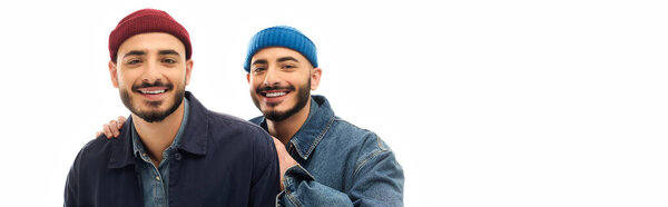 Two handsome twin brothers wear stylish outfits and hats, enjoying each others company playfully.