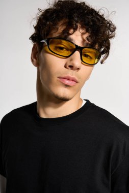 Kıvırcık saçlı, sporcu, sarı güneş gözlüklü bir genç stüdyoda..