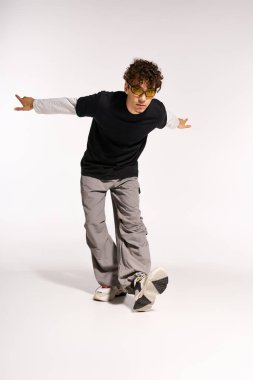 Güneş gözlüklü genç, kıvırcık saçlı bir adam parlak bir stüdyoda şık kıyafetini sergiliyor..