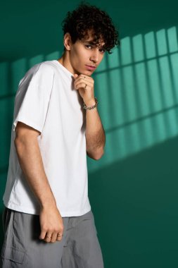 Curly-haired man poses confidently in a trendy outfit against a colorful backdrop.