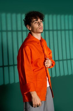 Kıvırcık saçlı şık bir genç modern bir stüdyoda poz verirken şık bir kıyafet sergiliyor..