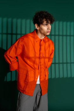 Kıvırcık saçlı şık genç bir adam yeşil bir stüdyoda poz veriyor..