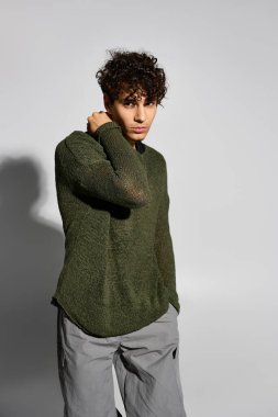 Kıvırcık saçlı genç bir adam modaya uygun giyinmiş, modern moda tarzını sergiliyor..