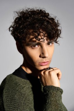 Şık kıvırcık saçlı ve şık kıyafetli genç bir adam şık bir stüdyo odasında duruyor..