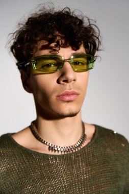 Kıvırcık saçlı genç bir adam, stüdyoda poz veren modaya uygun bir kıyafete güvendiğini ifade ediyor..